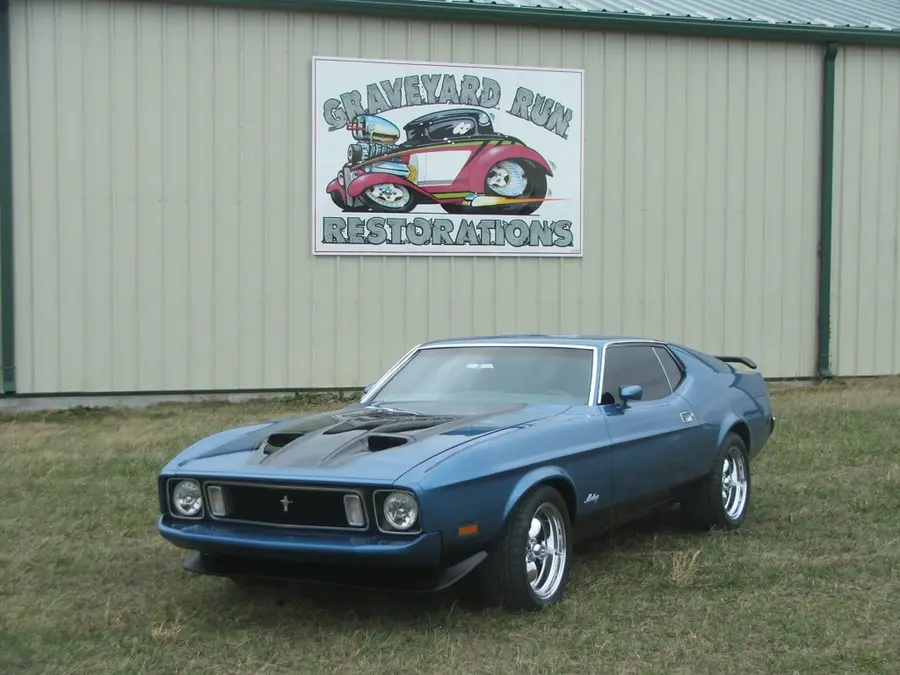 A blue restored muscle fastback under the shop sign.