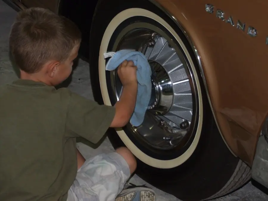 A young boy polishing the whitewall wheel of a restored Nash on the shop floor