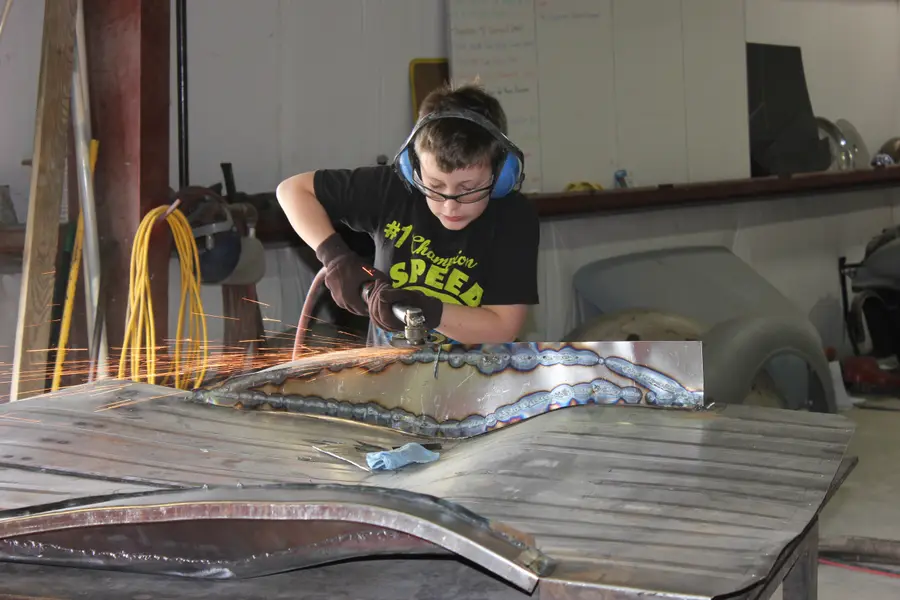 A young apprentice in ear protection grinding metal on a panel, sparks flying