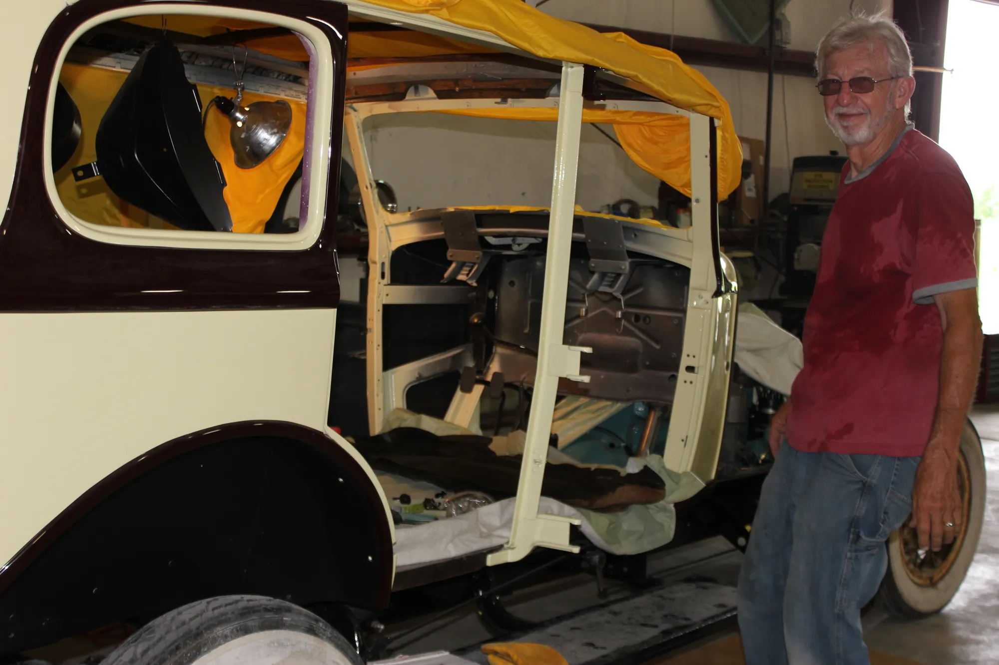 A craftsman standing in the open shop doorway among cars in progress
