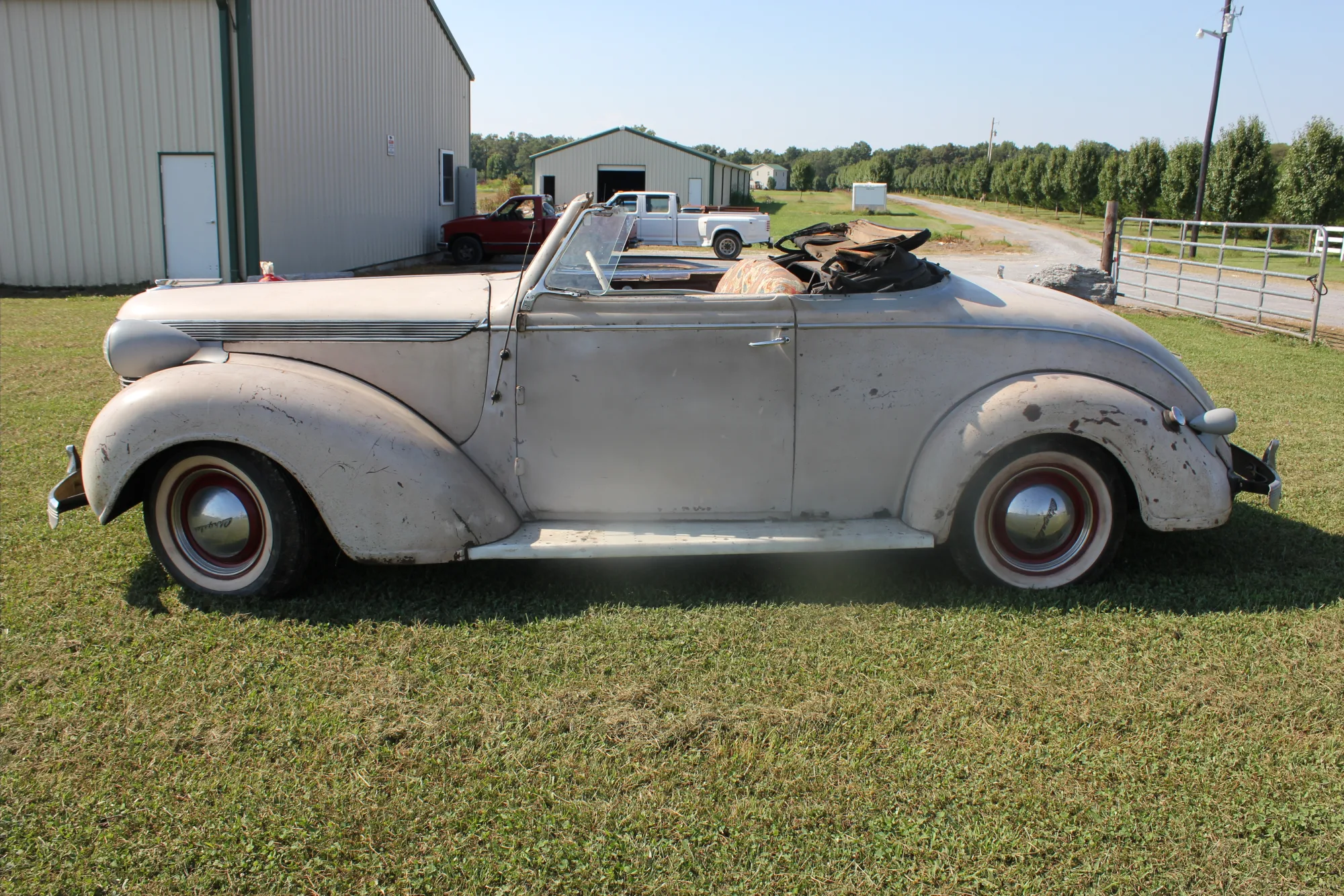 The Imperial roadster as found — weathered, faded paint, on the grass at the farm.